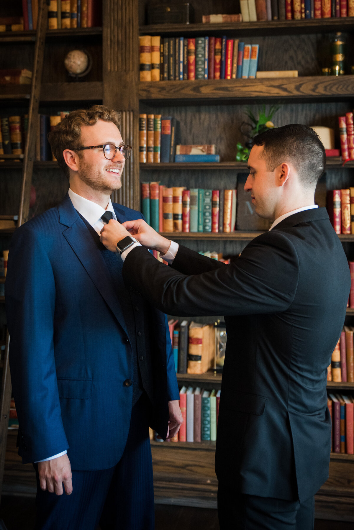 A groom's best man helps him adjust his tie in the library at The Manor House in Littleton, Colorado.