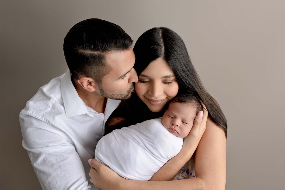Mom holding newborn baby boy and dad embracing them both with arms wrapped around them.
