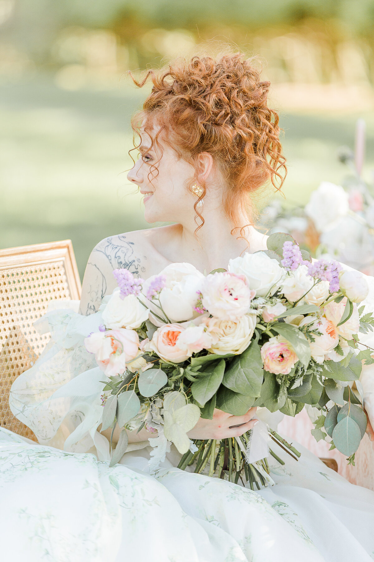 Bride is captured at a Parisean styled shoot holding a large bouquet. Her red hair upswept and looking over her shoulder. Captured by Lia Rose Weddings, Destination Wedding Photographer.