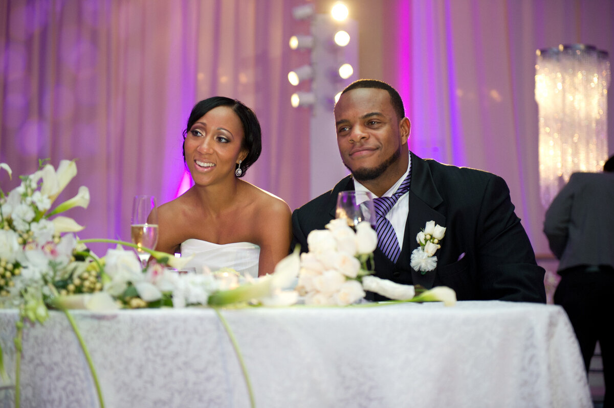 During wedding reception, bride and groom smiling and listening to someone