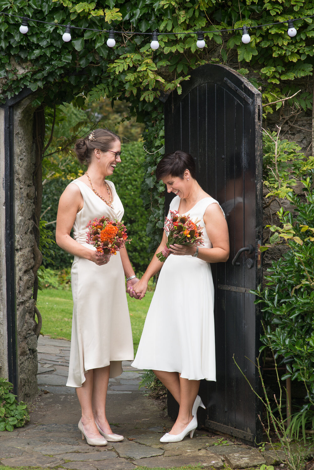 two brides holding hands at garden gate with fairy lights