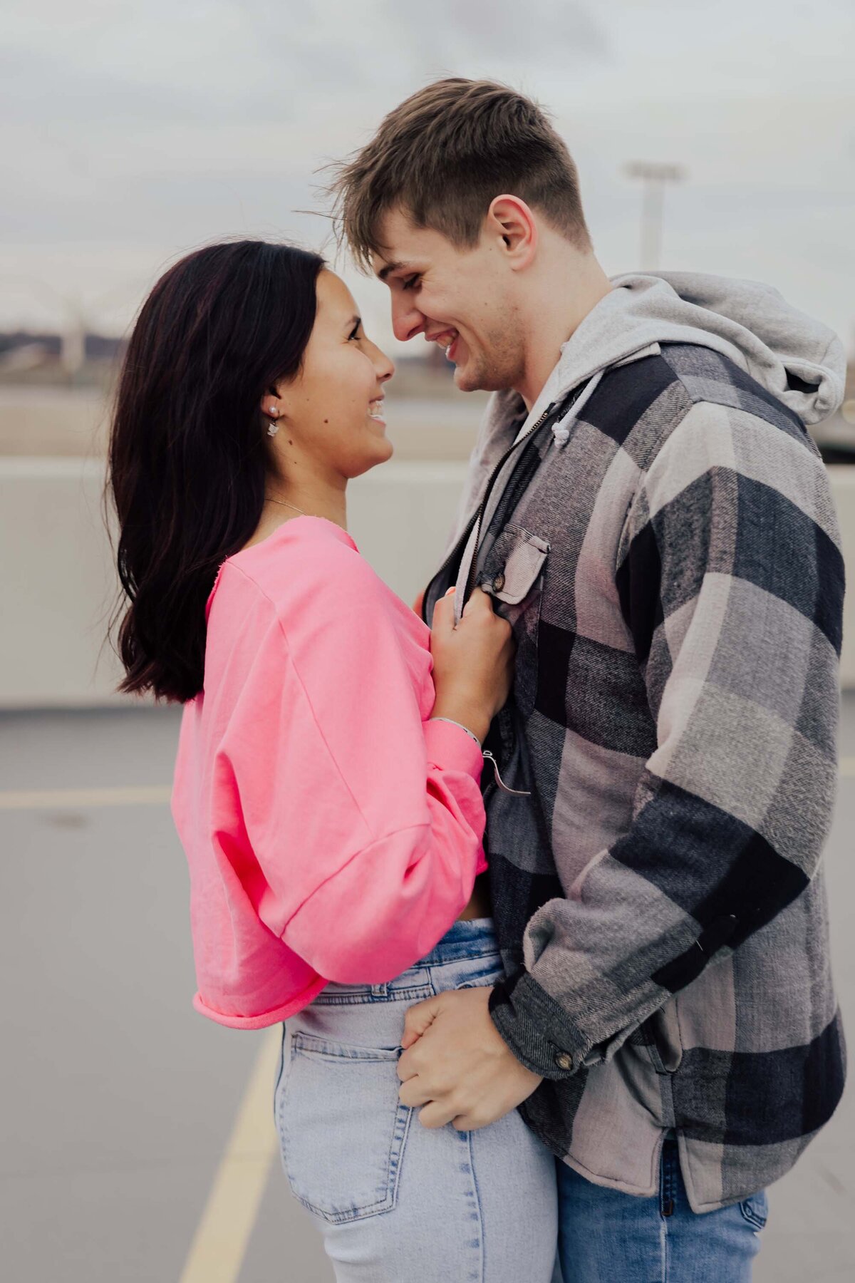 Maddie Rae Photography couple on the top of a parking garage. standing face to face. she is pulling him in by his jacket and he is pulling her in by her jean belt loops