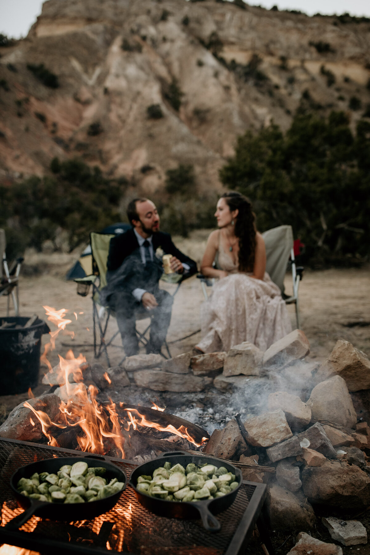 bride and groom sitting by a camp fire