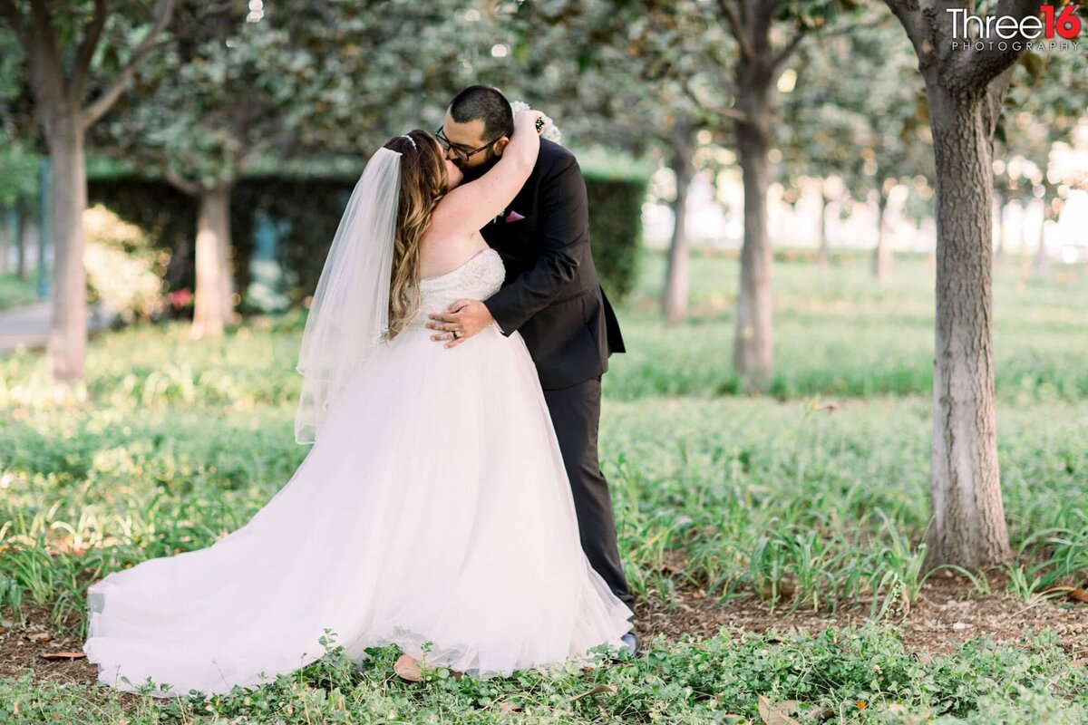 Bride and Groom share a romantic kiss under a tree in front of the hotel wedding venue