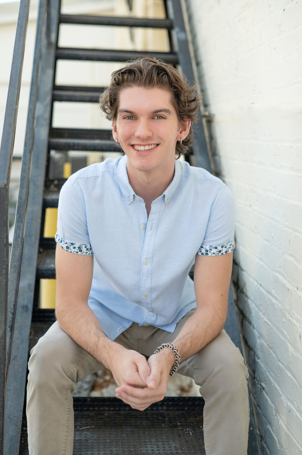 High school senior boy sitting on industrial stairs smiles at camera.