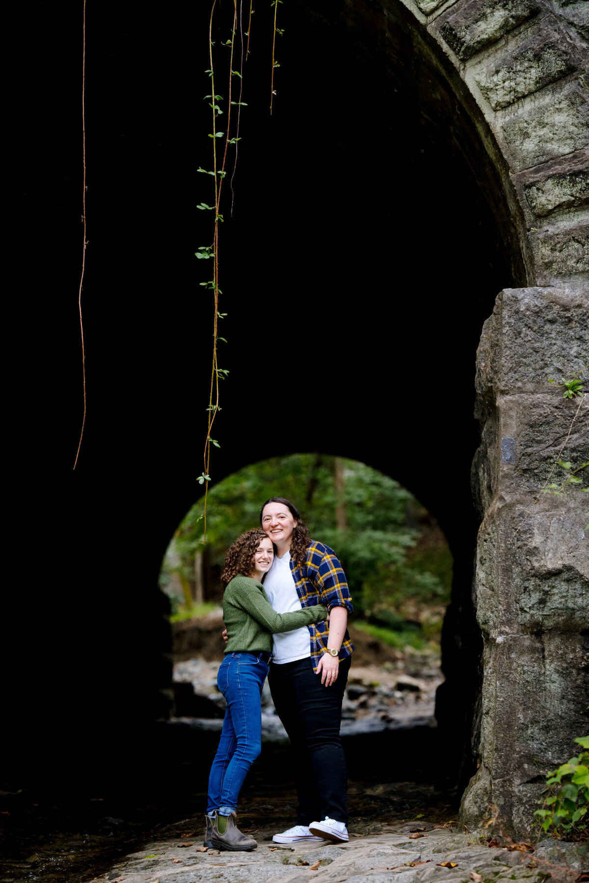 A couple hugging while standing under a stone bridge.