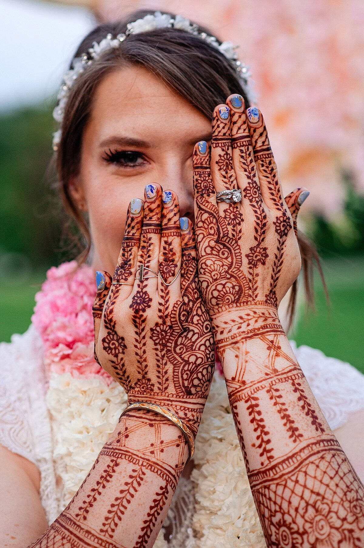 Bride shows off the henna mendhi she got on her hands for her Nashville Elopement at Ravenswood Mansion. She is also wearing a pink and white varmala garland, gold wedding bangles and an oval cut diamond engagement ring with her platinum wedding band.