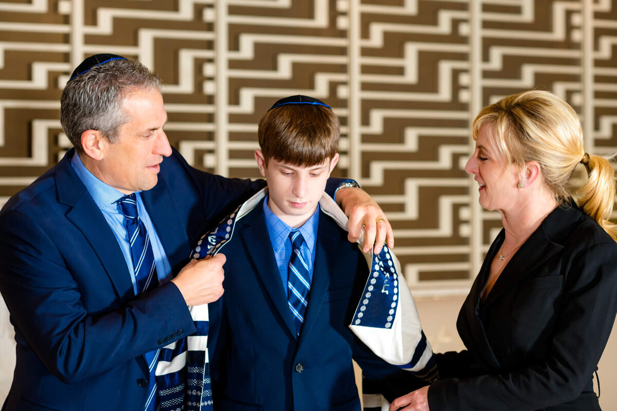 A mother and father help their son put on his tallit in the temple for his Bellevue Bar and Bat Mitzvah Photography