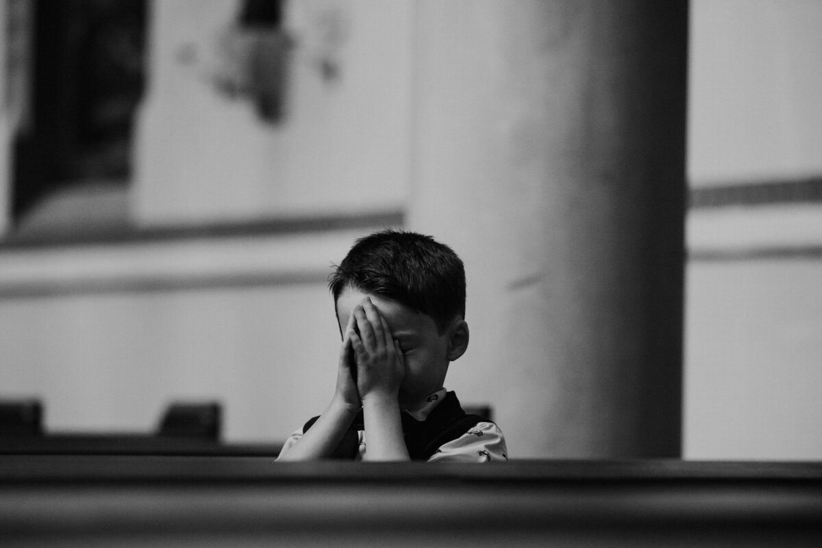Black and white photo of child folding hands over face in church
