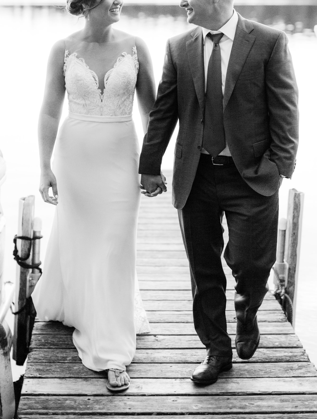 bride and groom walk hand in hand down dock to sherwood forest minnesota