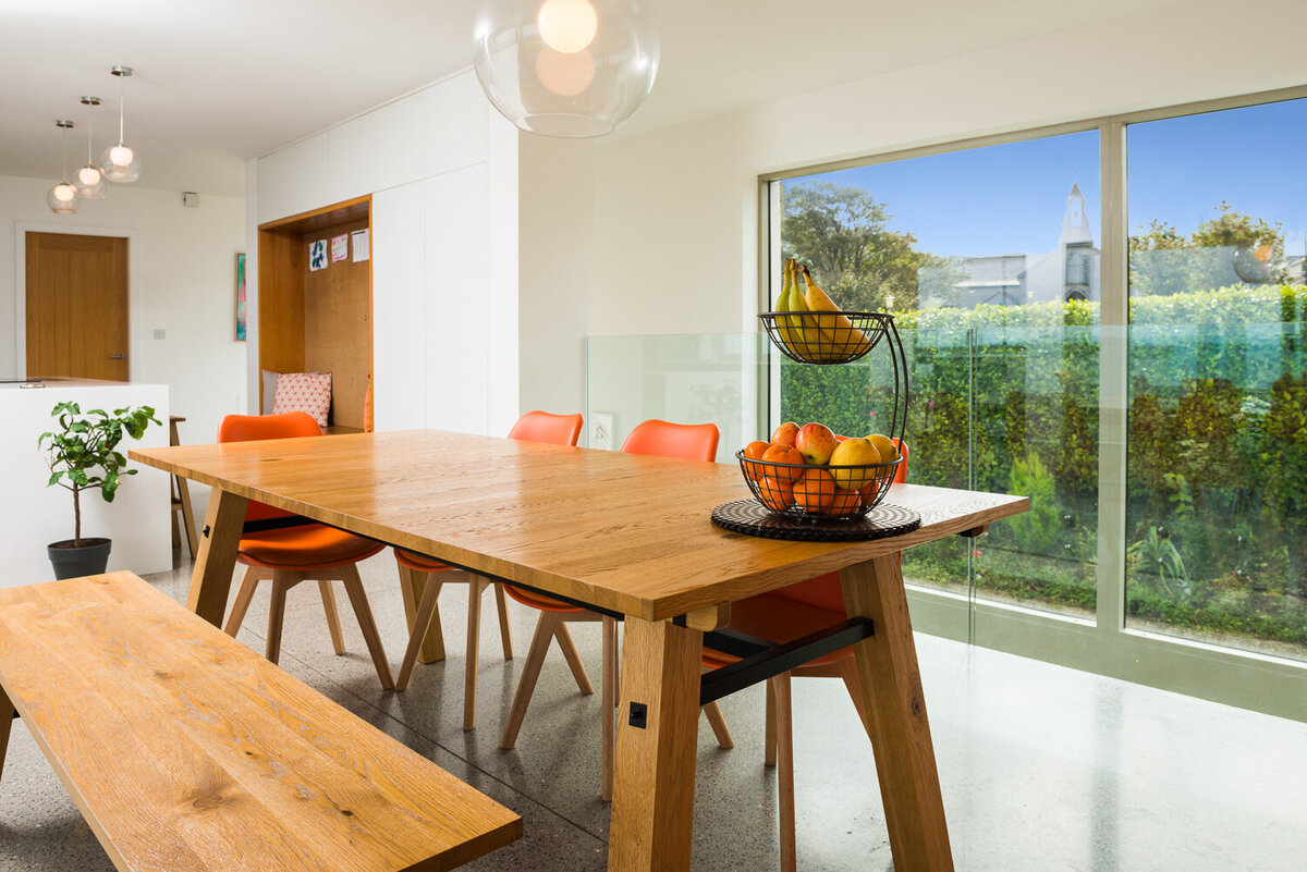 Wooden kitchen table and bench with orange chairs and floor to ceiling window