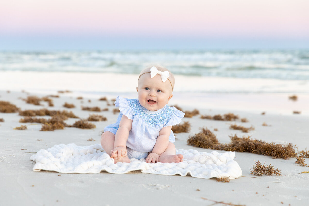 A small baby sitting on a blanket at the beach