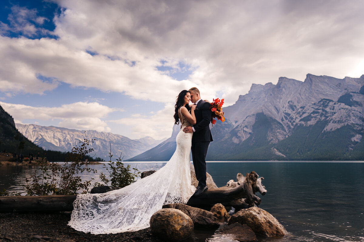 This couple shares a tender and intimate moment during their elopement at Lake Minnewanka in Banff, surrounded by the breathtaking beauty of nature.