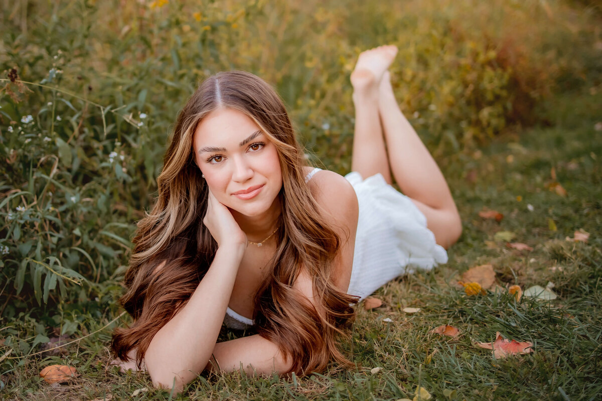 A beautiful high school senior laying on the ground on her belly propped up with her hand under her chin and posing for her Senior Photos.