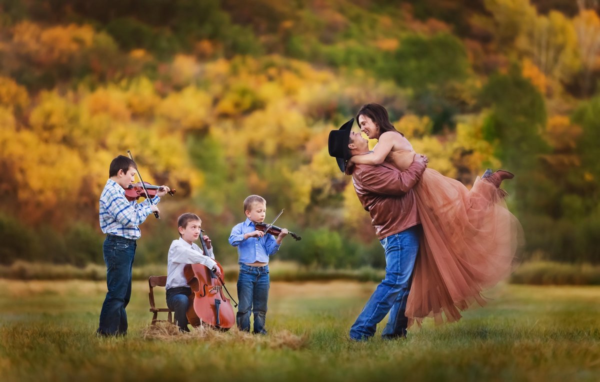 An engaged couple dancing in the mountains with three little boys serenading them with their violin, cello, and viola.