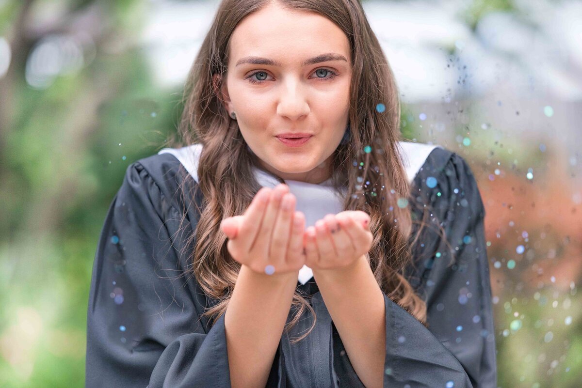 High school graduate blowing glitter at her cap and gown photos