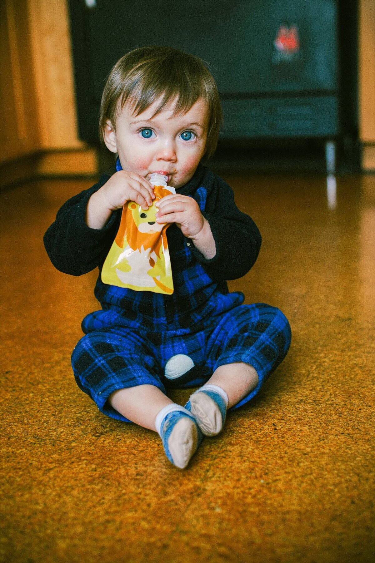 headshot of toddler sitting on kitchen floor eating a squooshy in Truckee, product lifestyle photography