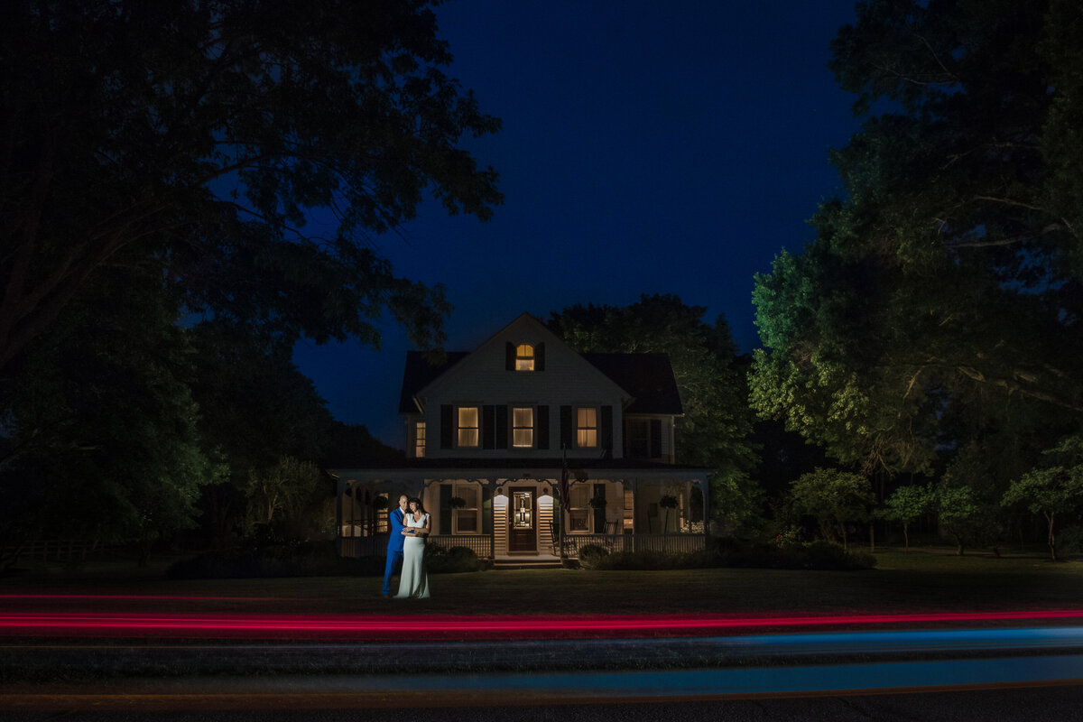 A bride and groom standing outside of a large house at dusk.