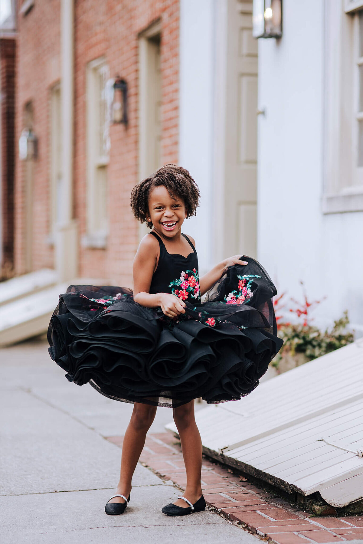 African American girl with brown curly hair spinning and laughing while holding a black floral dress in Fells Point in Baltimore Maryland