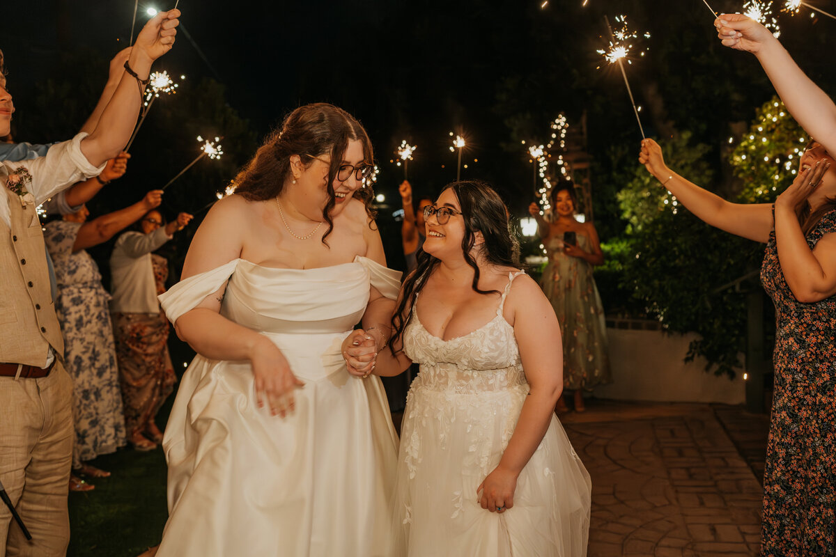 A newlywed couple holding hands and walking through a tunnel of their guests holding sparklers 
