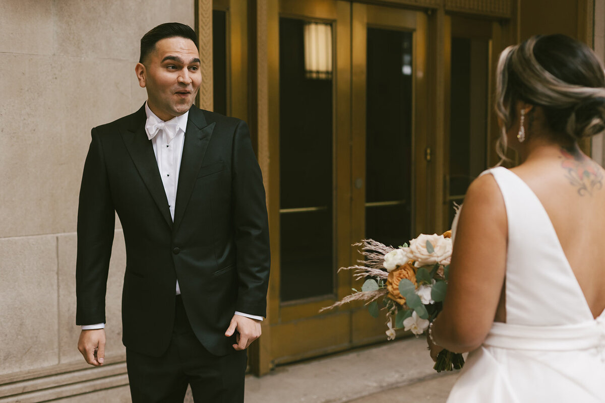 Groom stares in awe of elegant bride holding bouquet at Chicago wedding first look.