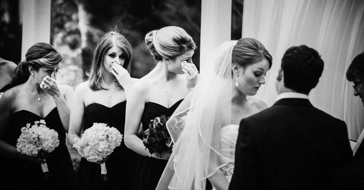 Emotional black and white photo of bridesmaids wiping tears during the wedding ceremony, with the bride looking on