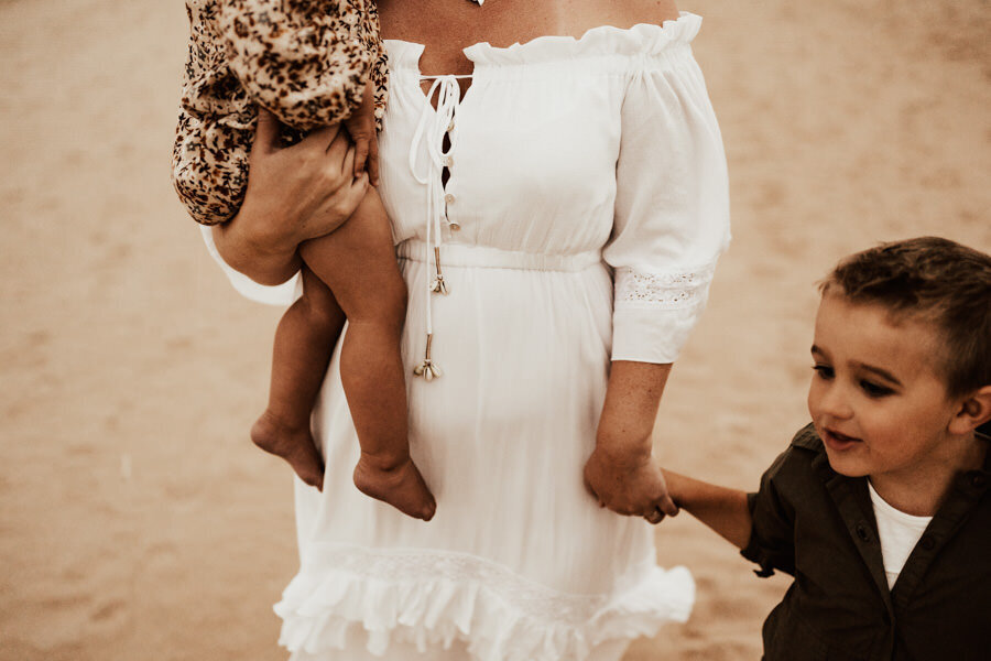 mamma har ett barn i famnen och håller ett barn i handen medan de går på stranden i halmstad