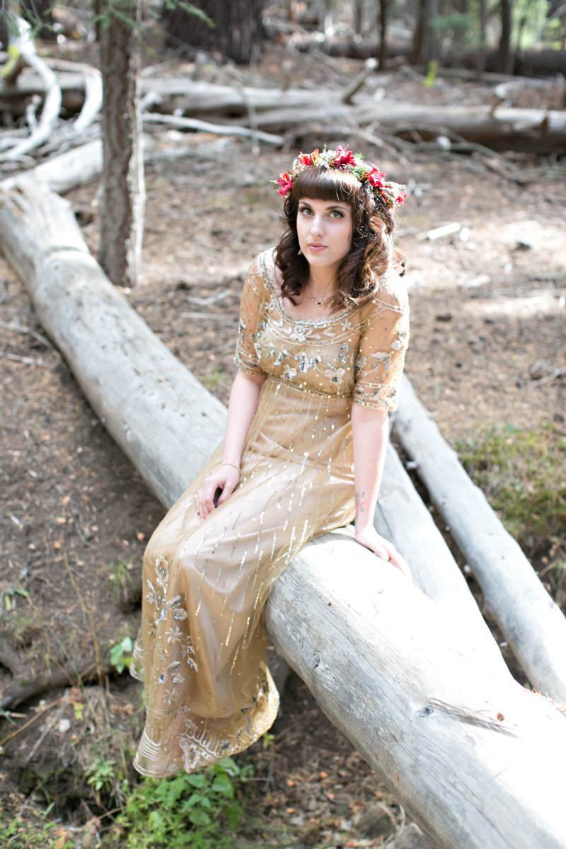 Bride wearing floral crown and gold Anthropologie wedding dress sitting on log