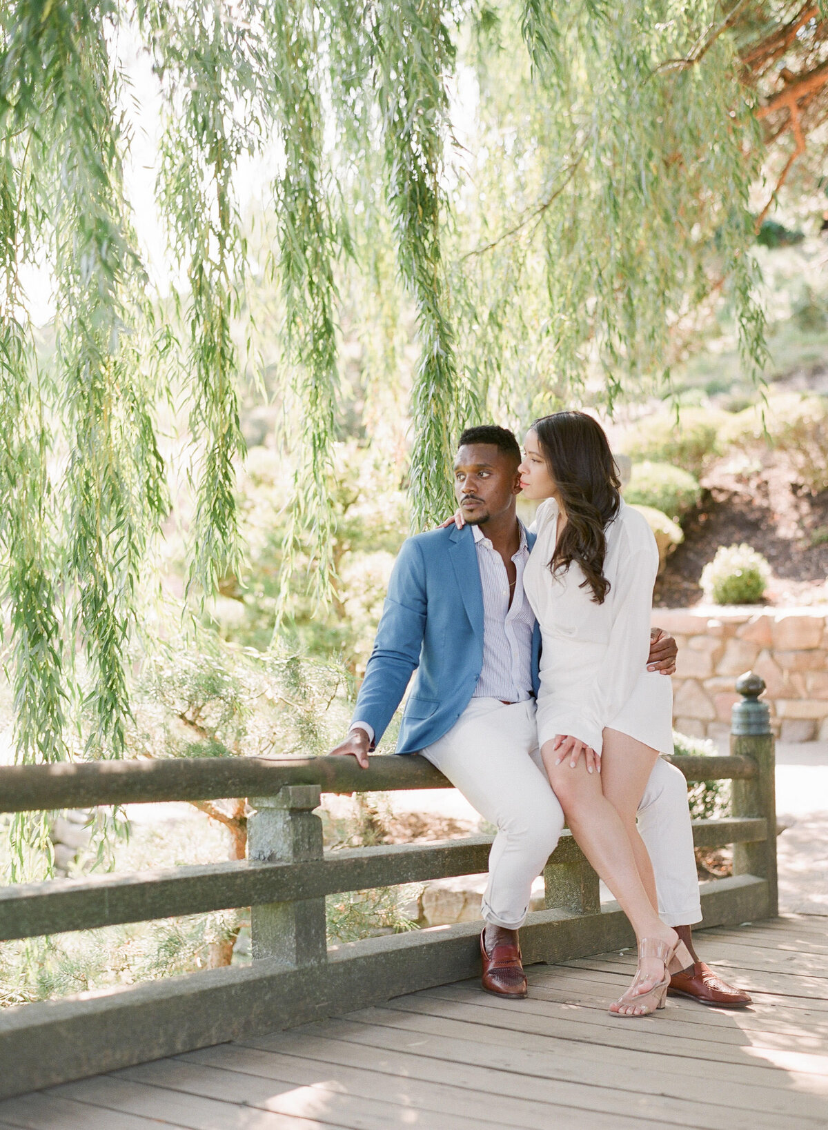 a couple standing under a willow tree in the botanic garden