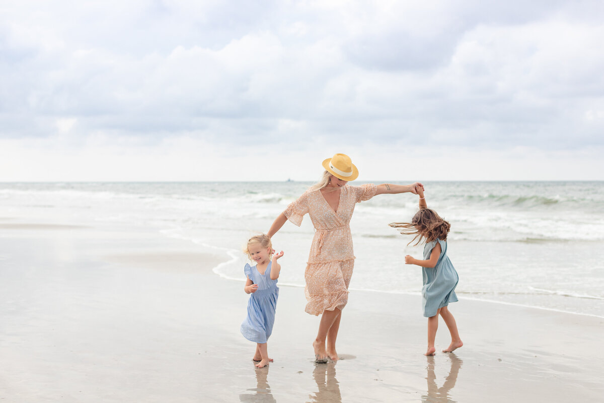 Mom and two girls twirling on the beach during a family session in Jacksonville