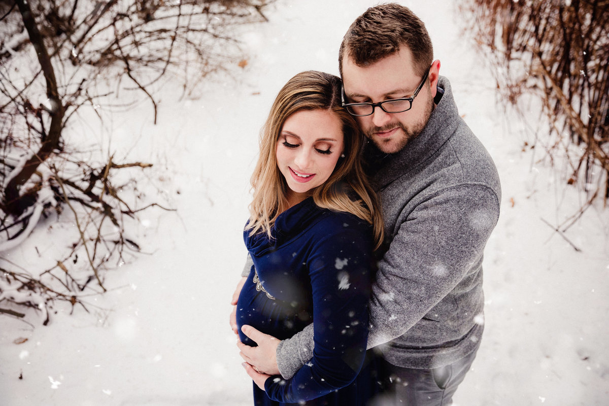 Expecting couple hugging in the snow