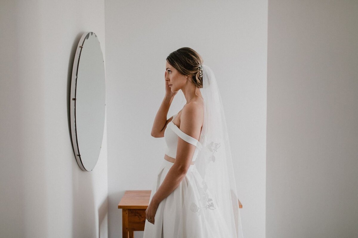 Bride looking in round mirror at her finished hair and makeup
