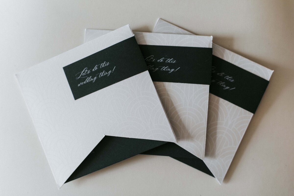 Various textured Ivory and white wedding stationery with a dark green label and cursive font.