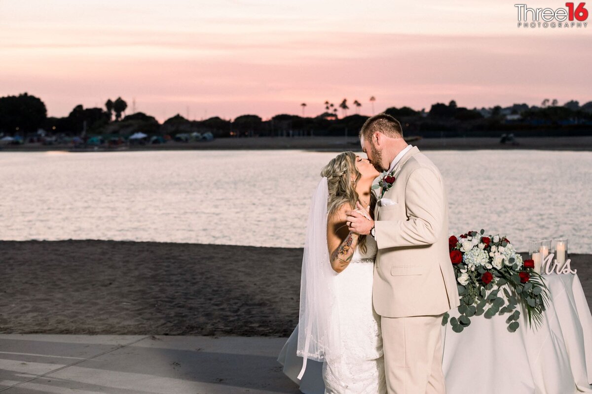 Bride and Groom share a kiss during their first dance as the sun sets in the back across the Newport Back Bay of Newport Dunes
