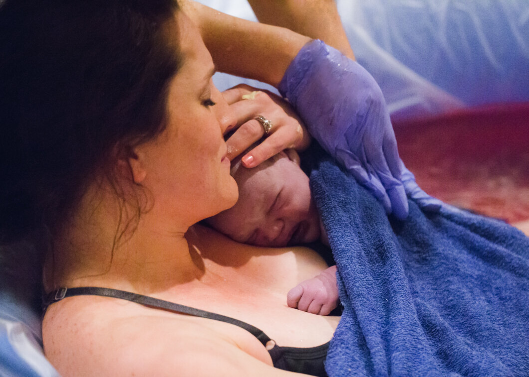 A new mother snuggles her brand new baby in a birthing tub. Birth story by Diane Owen.