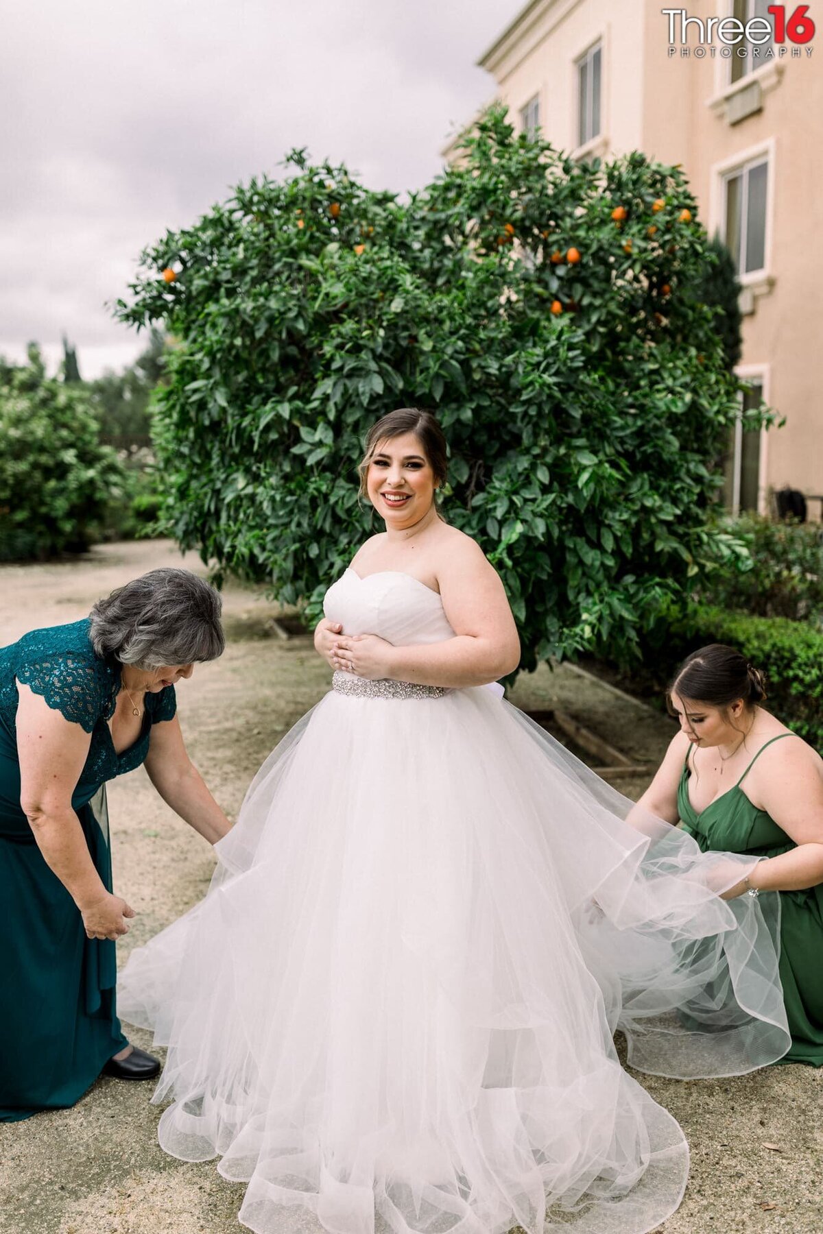 Bride having her dress train fanned out by her mother and bridesmaid before photos