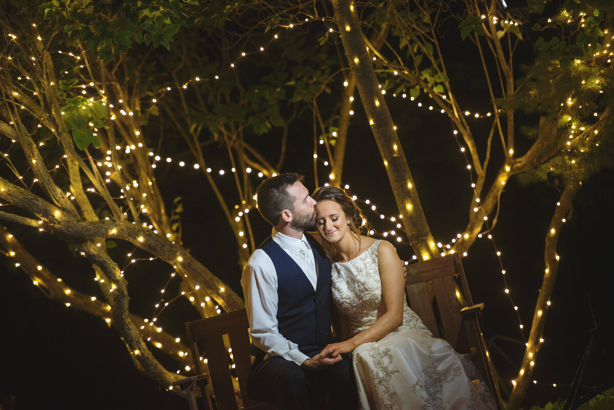Wedding couple kissing at night by twinkling lights.