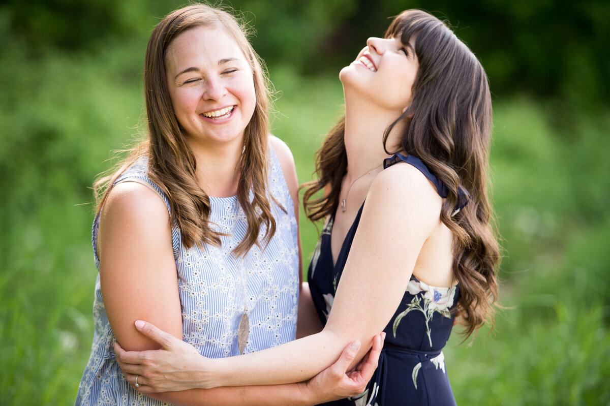two sisters hugging and laughing in a grassy filed captured by Ottawa Family Photographer JEMMAN  Photography