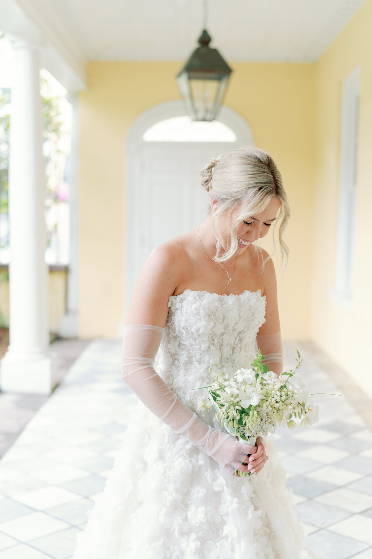William Aiken House bride in dress decorated with white flower design. Simple and small white and green flowers.  Blonde bride with hair up and bangs in face.
