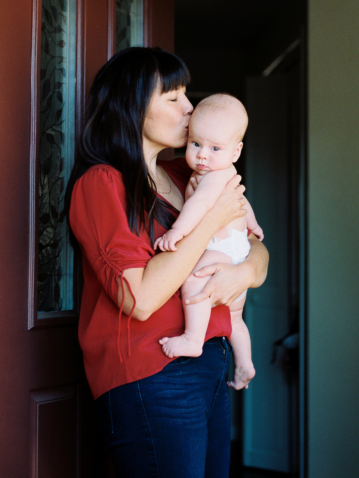 mom in red top kisses baby boy by front door