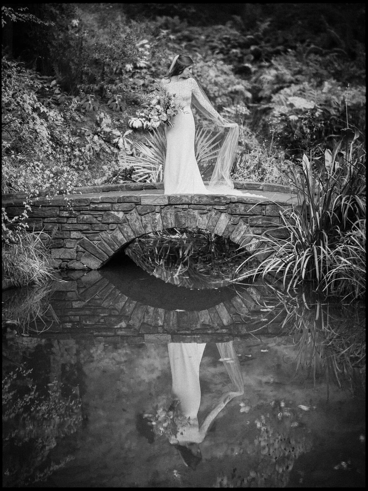 Image of a bride on a bridge reflecting in a small pond