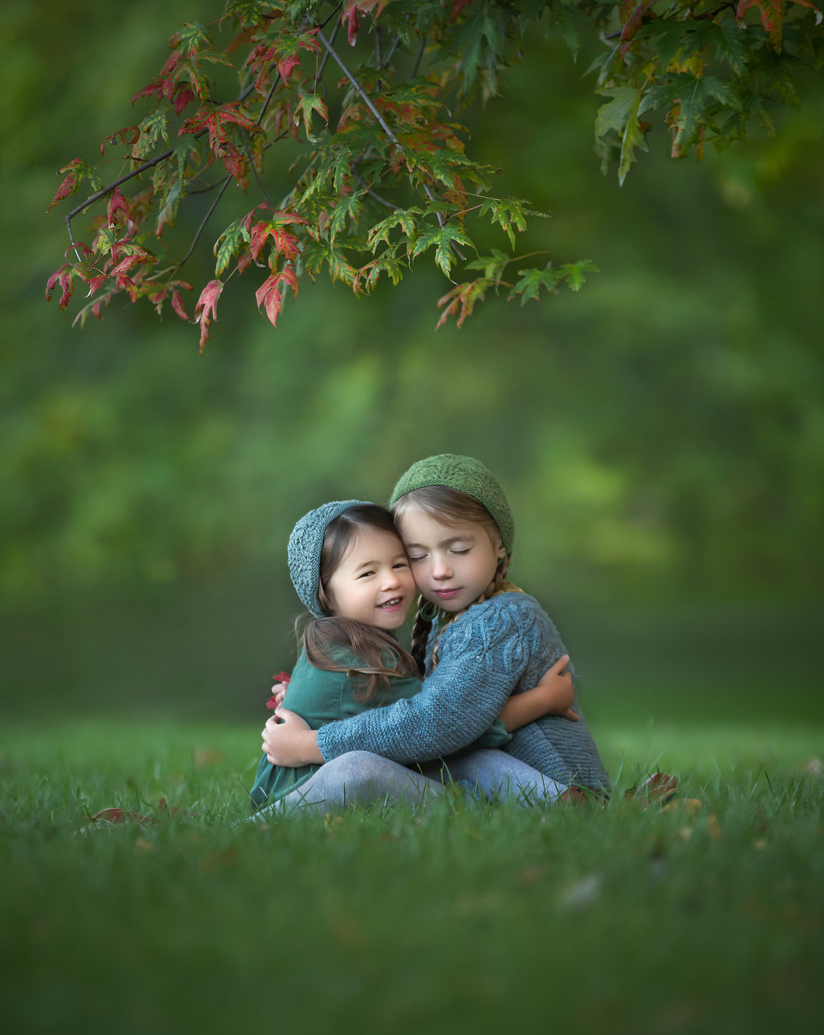 Two young sisters hugging while sitting under a low hanging maple tree in Ottawa.