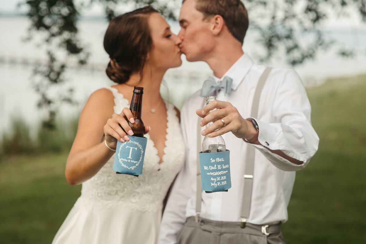 A bride and groom kiss with drinks in hand