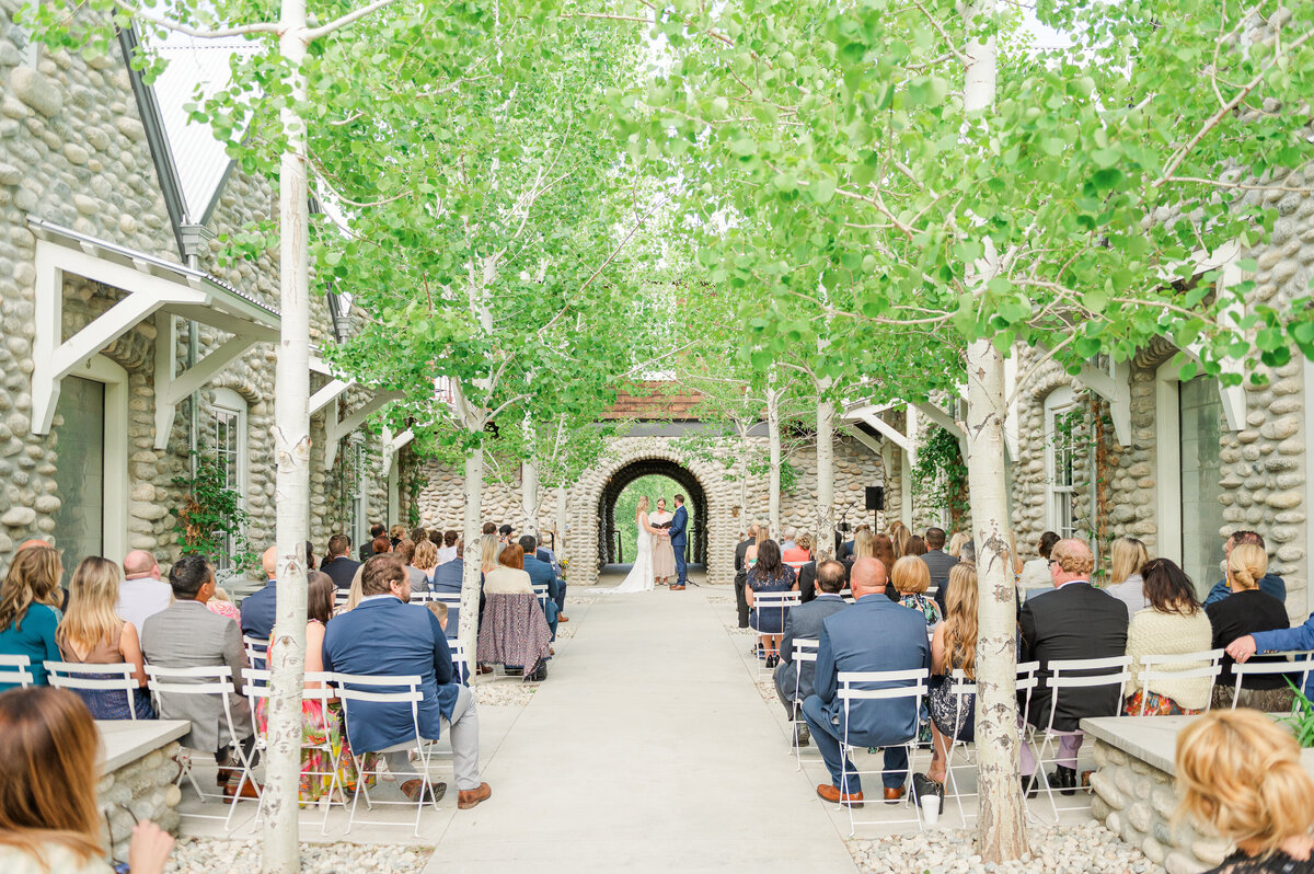Outdoor wedding ceremony in a European styled stone courtyard surrounded by aspen trees.