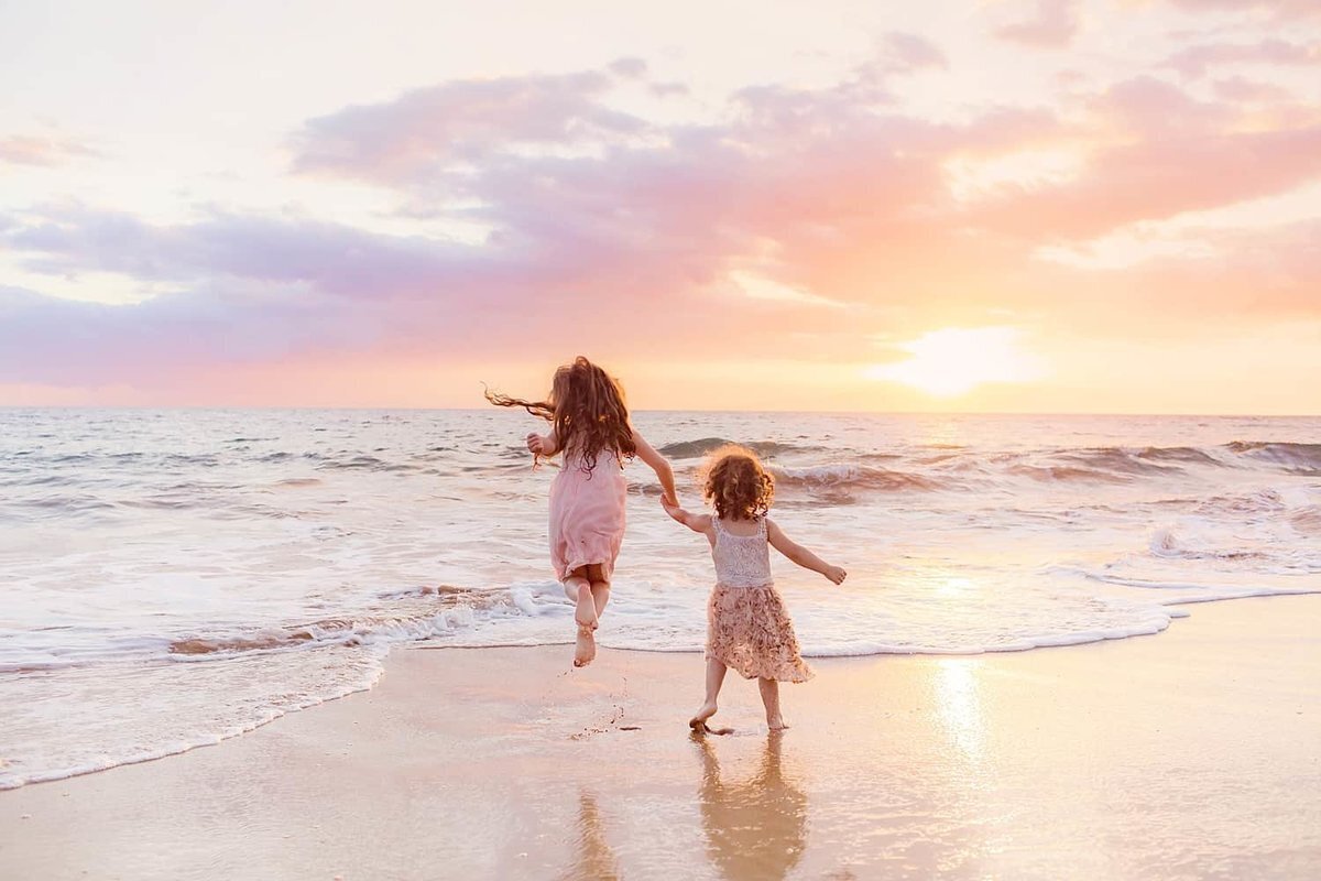 Young girls hold hands just before sunset on Maui as their family watches from the shoreline