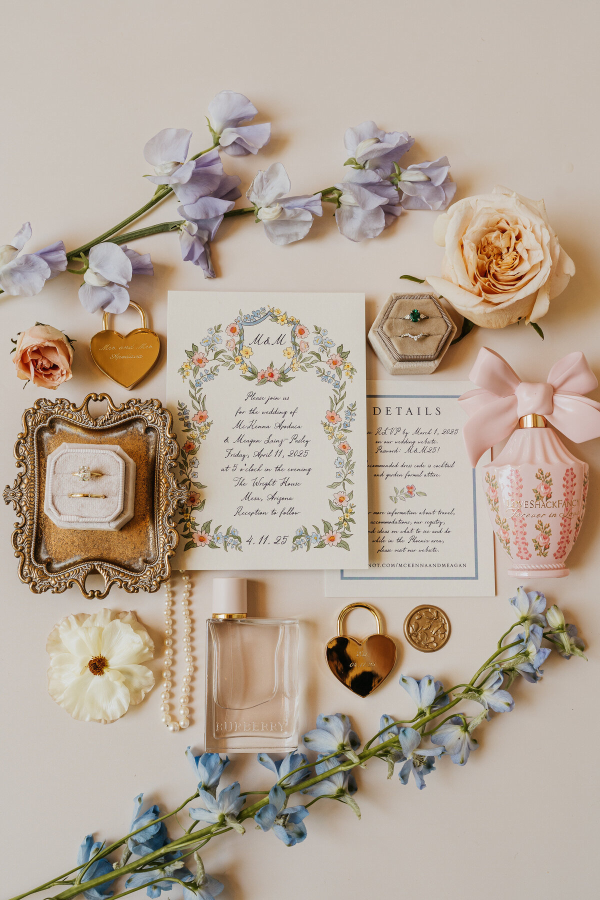 A flat lay showing off wedding invitations, jewelry, perfume, flowers and more