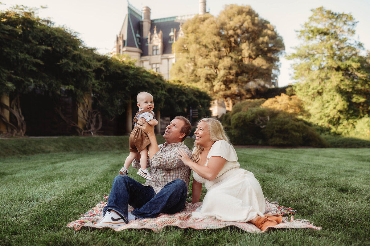 Family sits together on the lawn in front of Biltmore Estate during Family Photos in Asheville, NC.