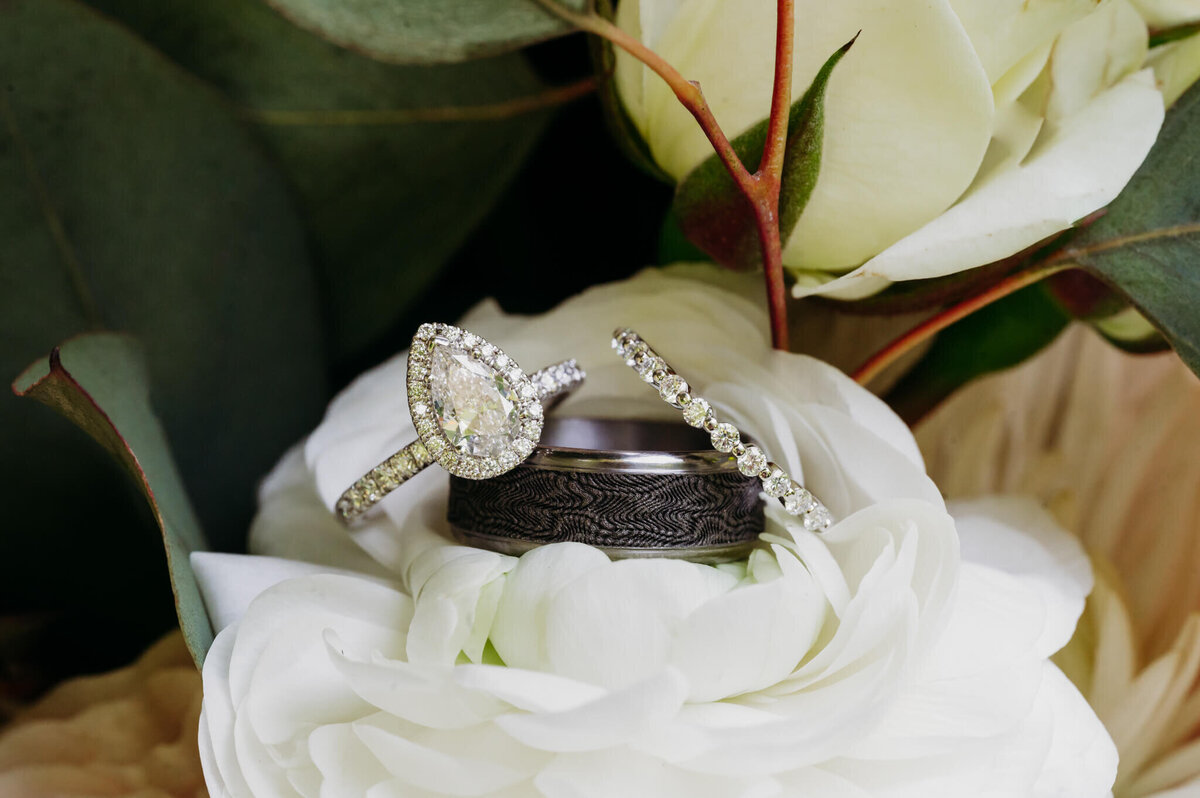 Photo of an engagement ring and wedding rings propped on a white flower