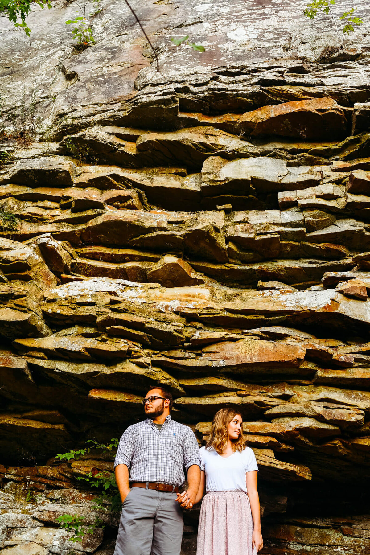 photo of a man and woman holding hands and looking away in front of a rock wall