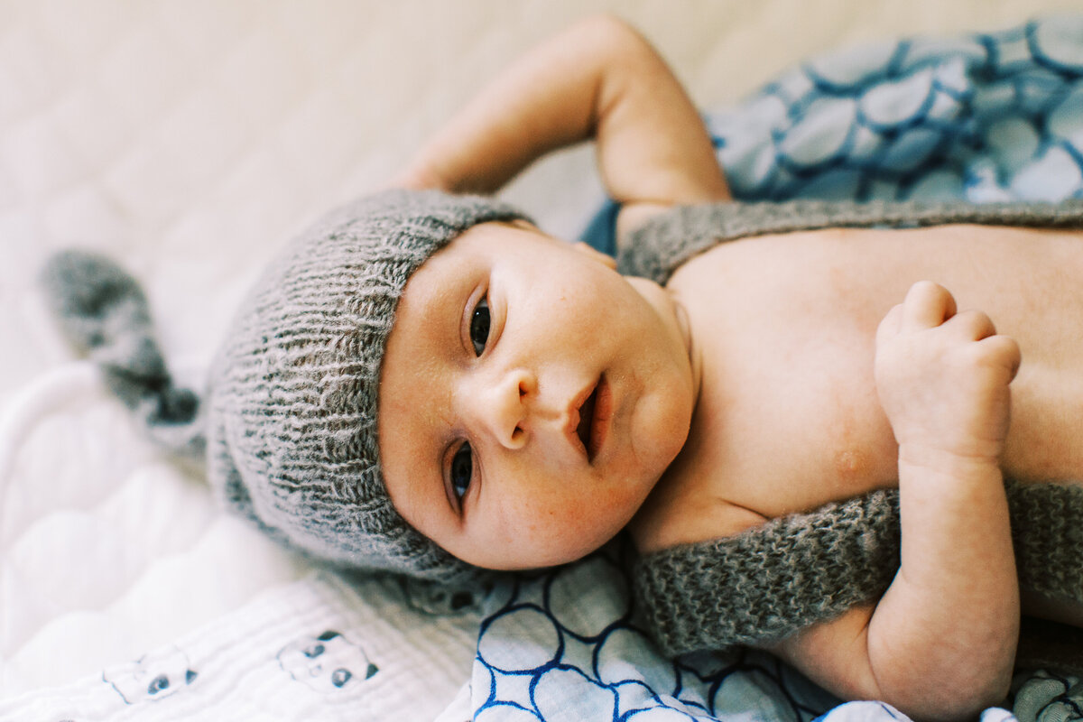 lifestyle baby portrait of newborn lying on crib and wearing a gray knit hat